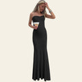 Woman in a black strapless gown standing on a staircase holding a glass.