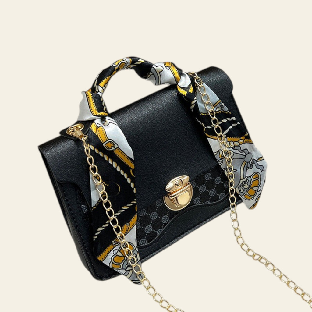 Black handbag with gold chain and decorative ribbon on a white fur surface
