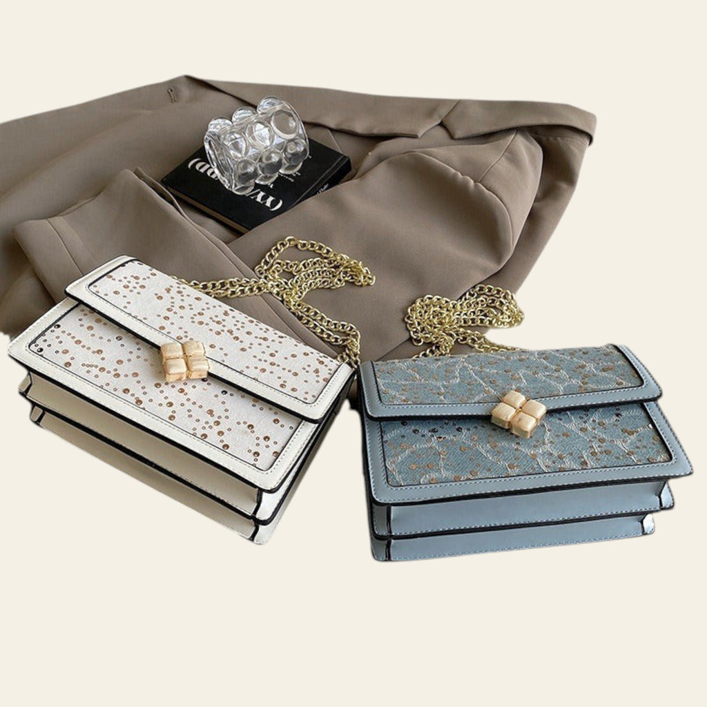 Two handbags with gold chains on a beige fabric background
