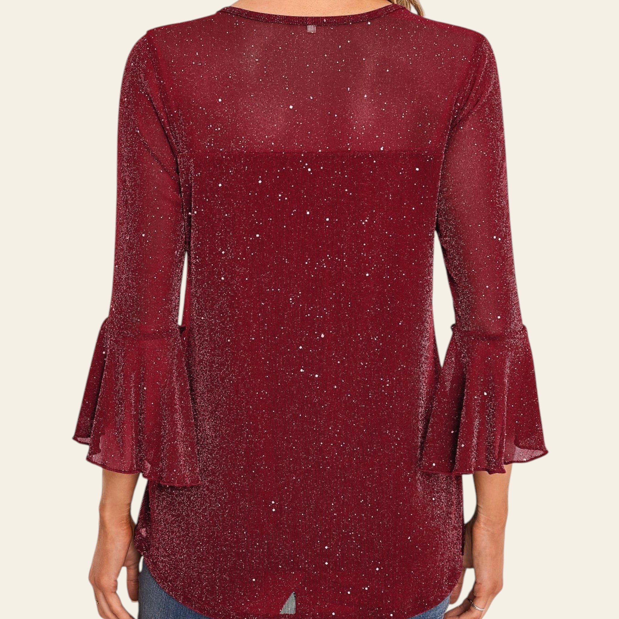 Woman wearing a burgundy ruffled blouse with a white decorative wall in the background