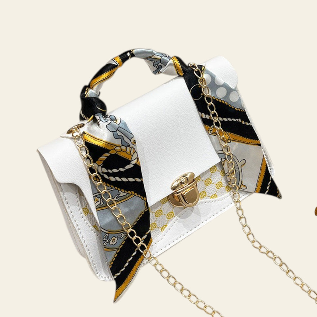 White handbag with gold chain and decorative scarf on a fluffy white surface