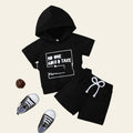 Black hoodie and shorts set with text on a wooden surface, accompanied by black sneakers.