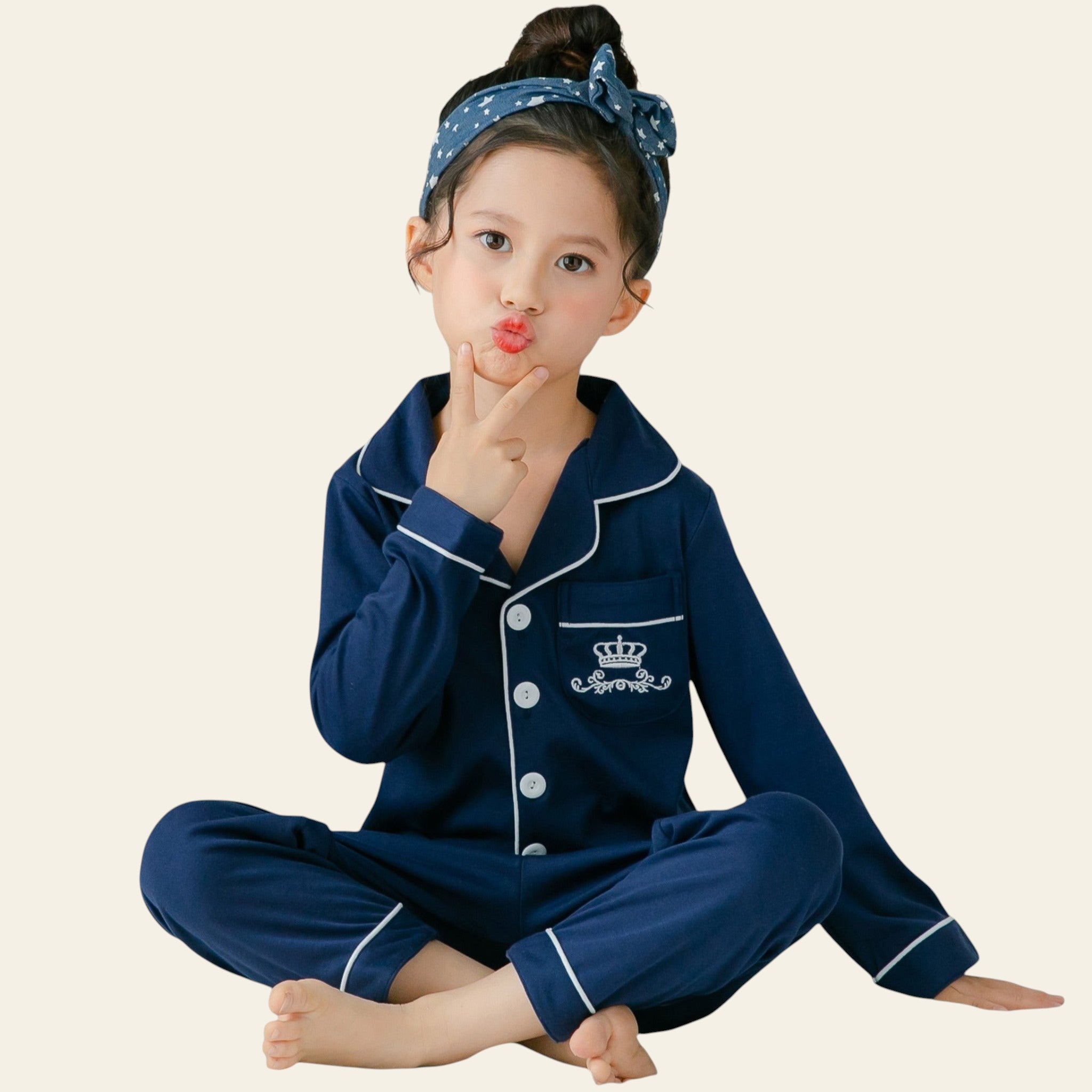 Child wearing navy blue pajamas with white buttons and trim, sitting on a bed.
