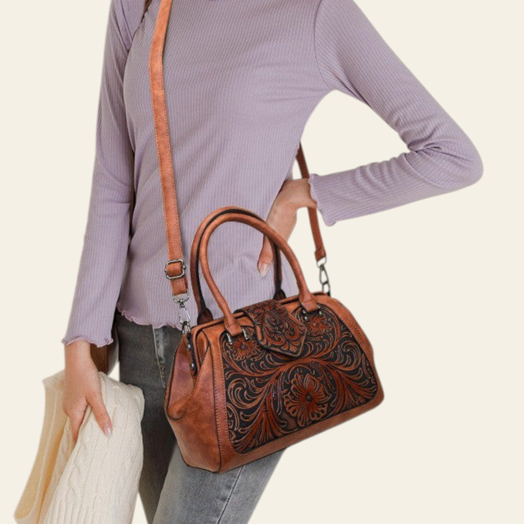 Person holding a brown leather handbag with intricate designs on a plain background