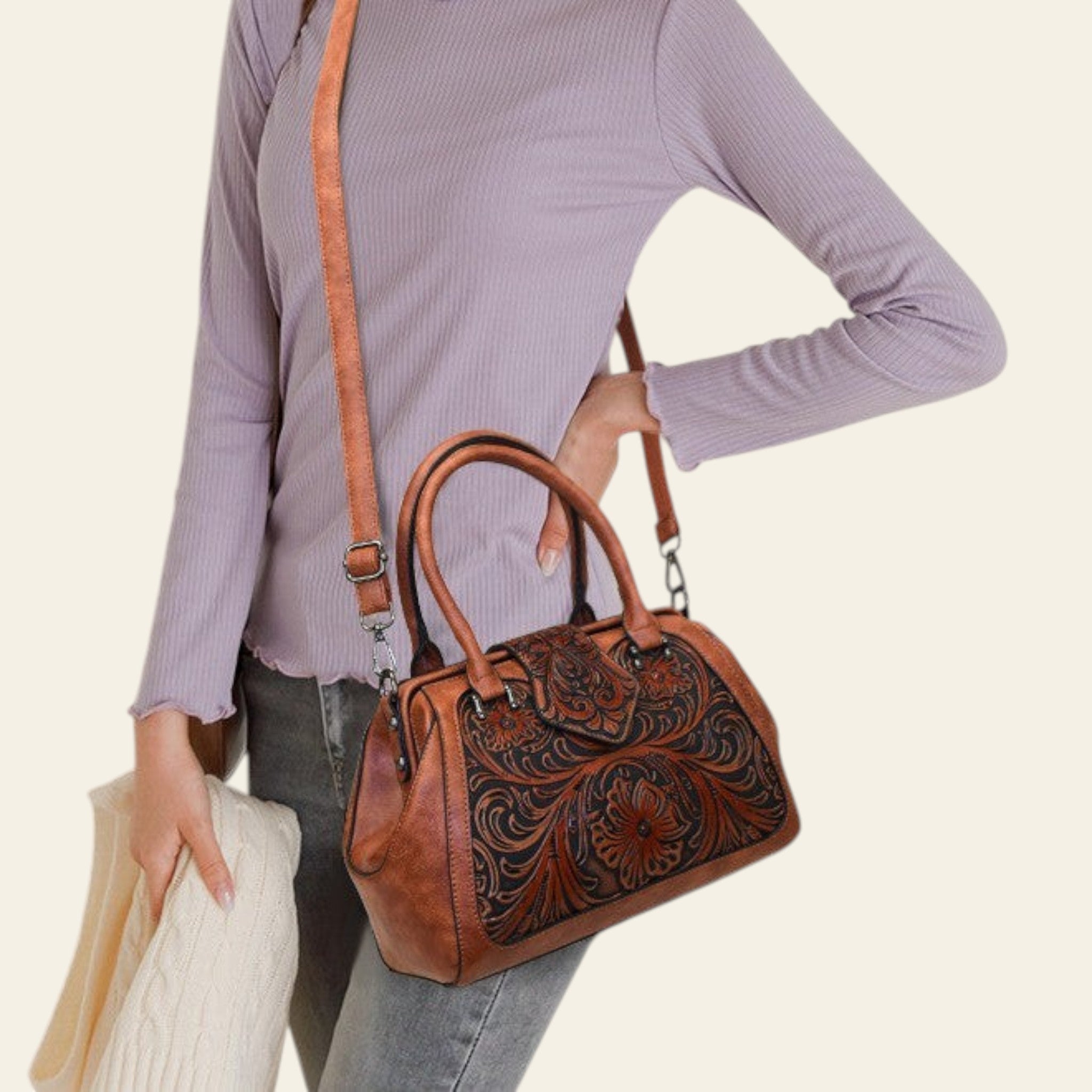 Person holding a brown leather handbag with intricate designs on a plain background
