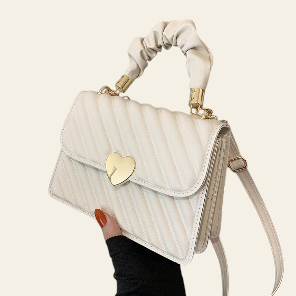 White handbag with a gold heart lock held by a hand on a magazine