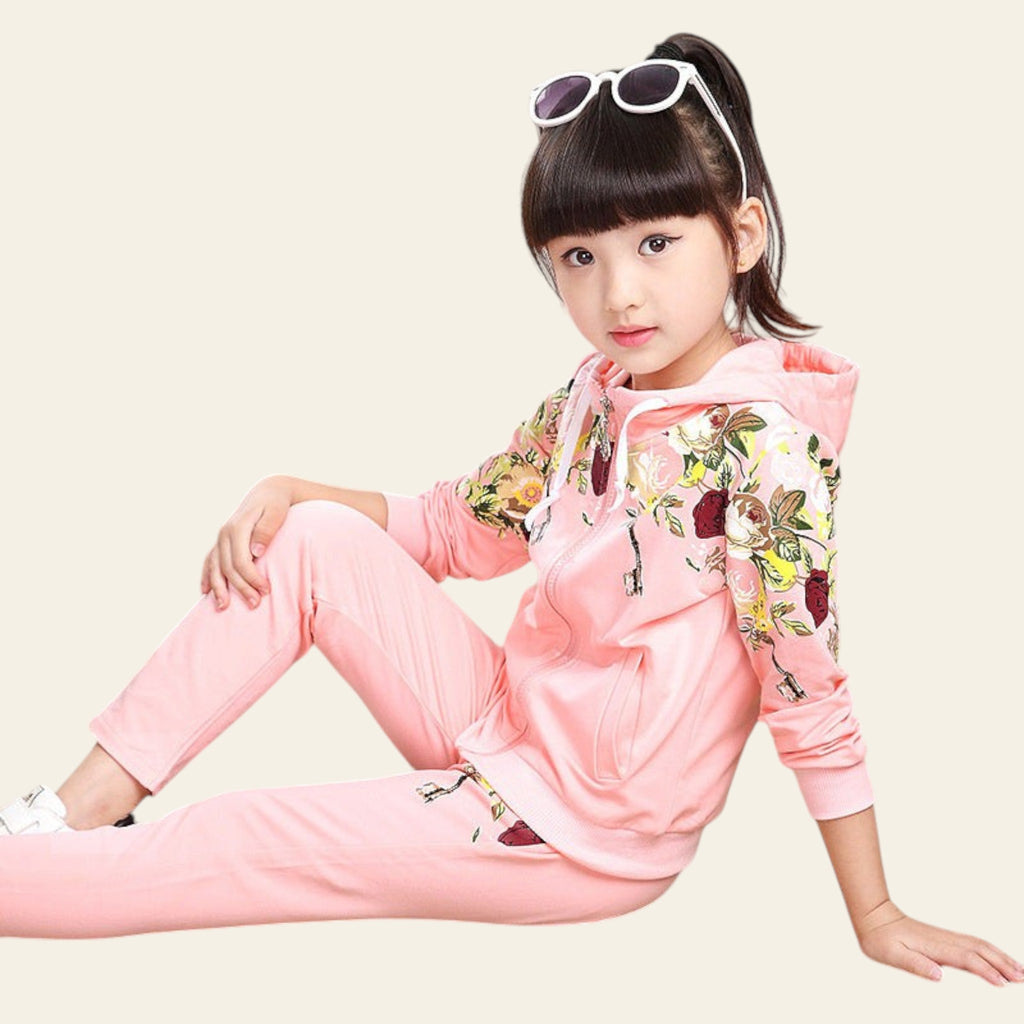Young girl in a pink floral tracksuit sitting on the floor.