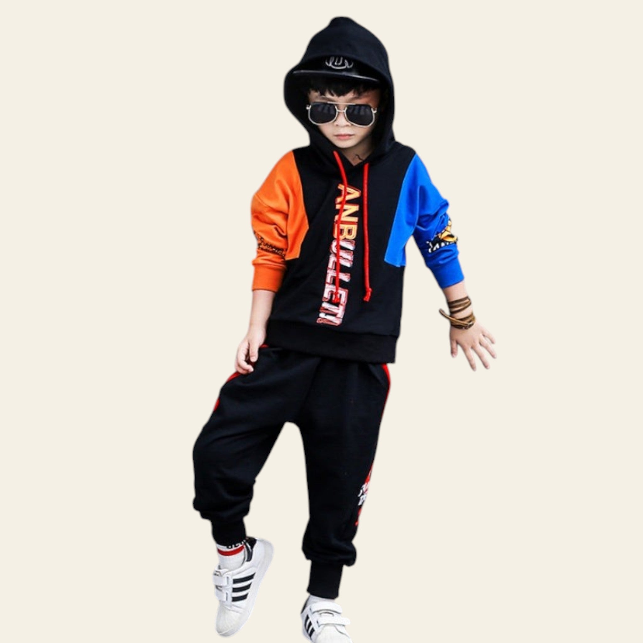 Child wearing a colorful outfit with a black hoodie and pants, standing against a gray wall with large black letters.