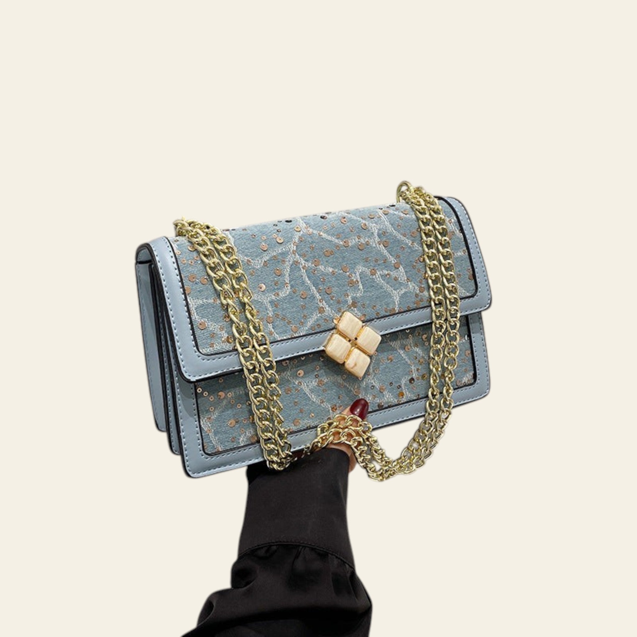 Blue handbag with gold chain held by a person in a white room.