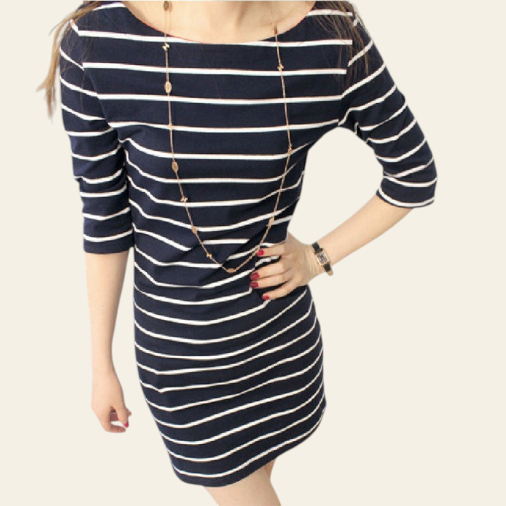 Woman wearing a navy and white striped dress with a gold necklace indoors.
