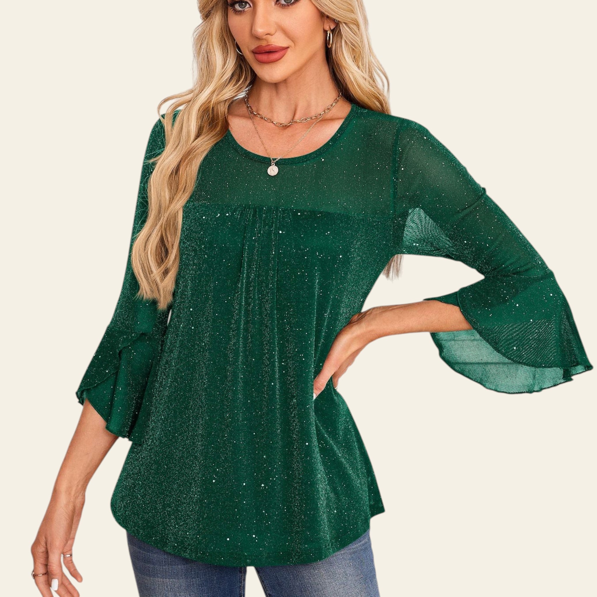 Woman wearing a green blouse with bell sleeves against a decorative white wall.