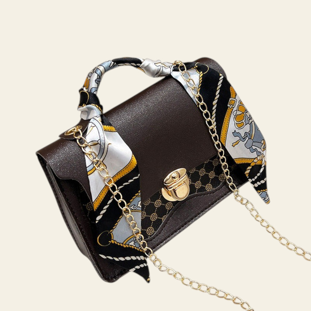 Brown handbag with gold chain and patterned scarf on a white surface