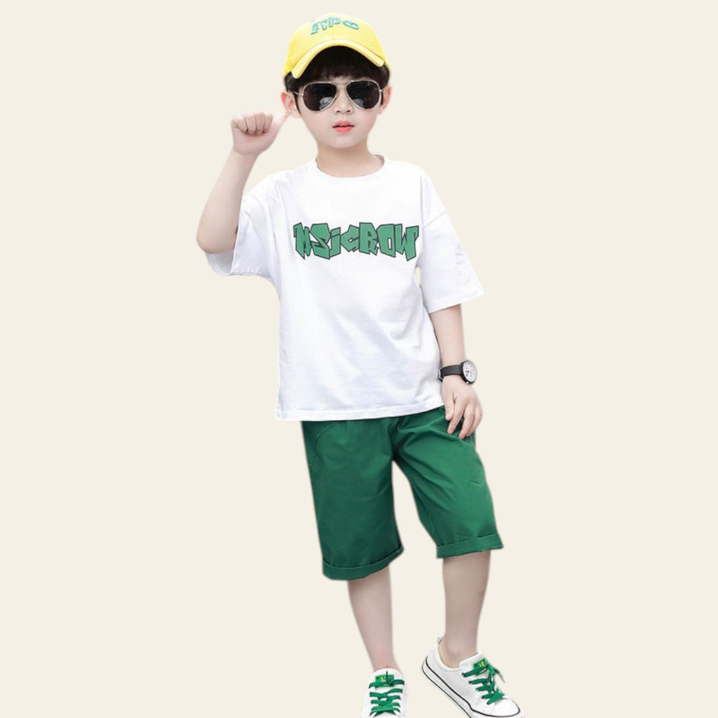 Child wearing a white t-shirt with green text, green shorts, and a yellow cap on a street.