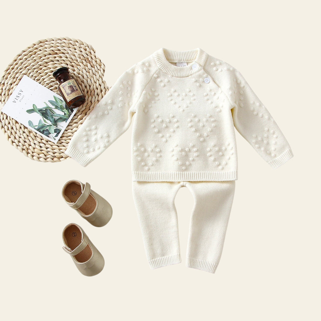 White knitted sweater and pants set with baby shoes on a light background
