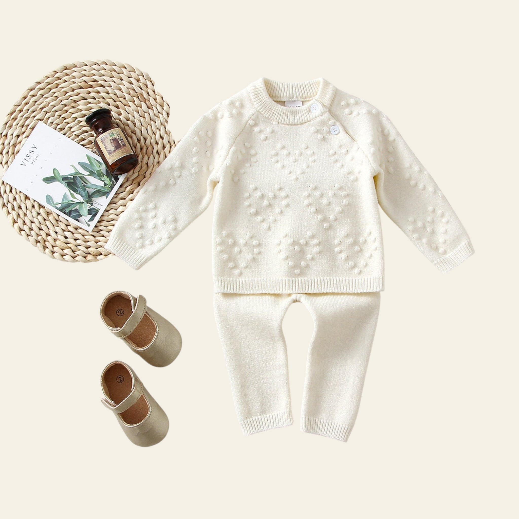 White knitted sweater and pants set with baby shoes on a light background
