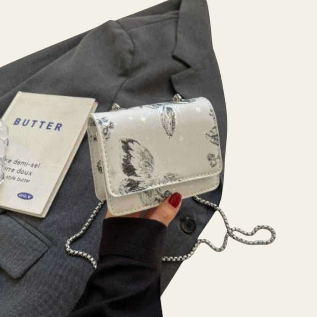 Handbag with butterfly design held by a person wearing a gray coat, with a 'Butter' magazine in the background.