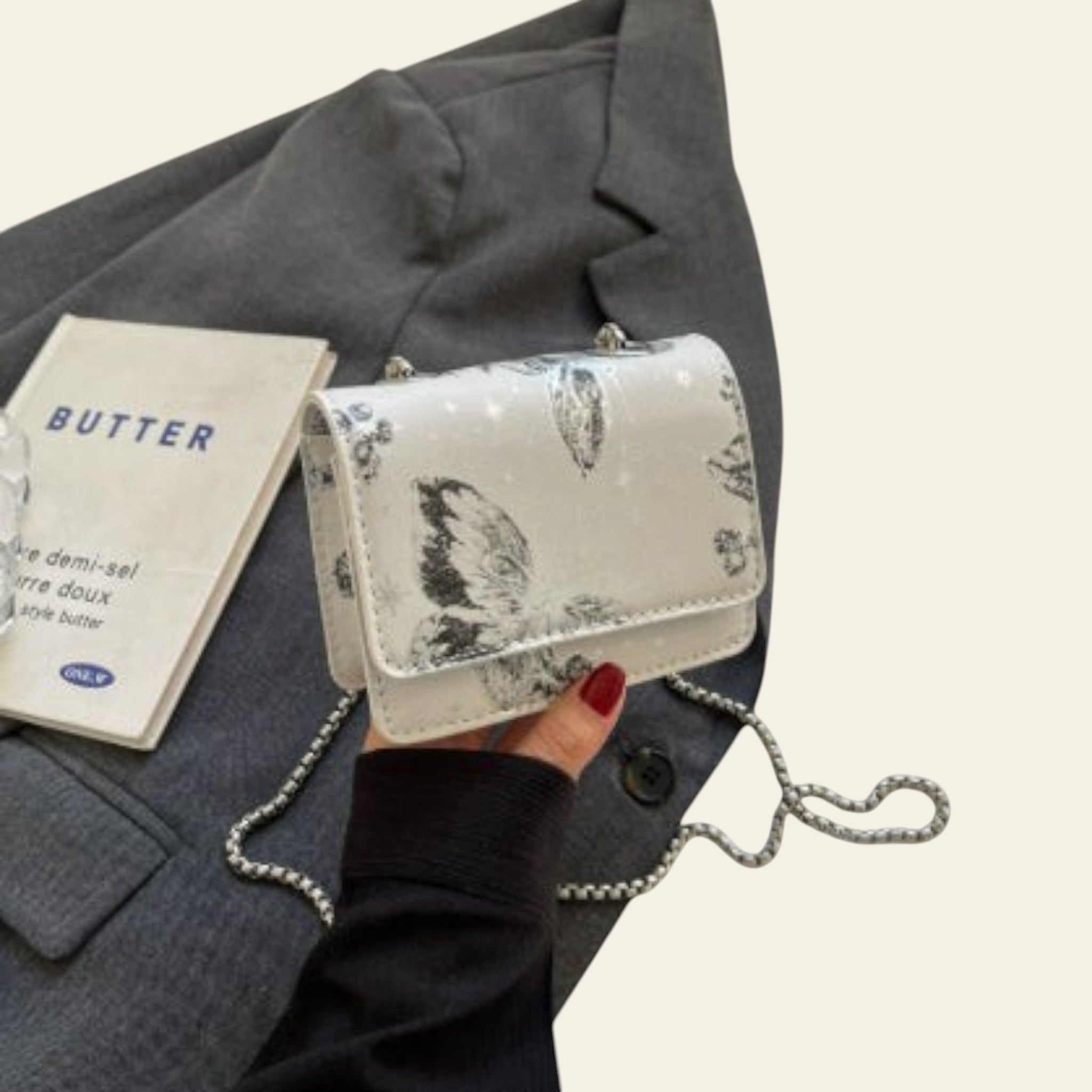 Handbag with butterfly design held by a person wearing a gray coat, with a 'Butter' magazine in the background.