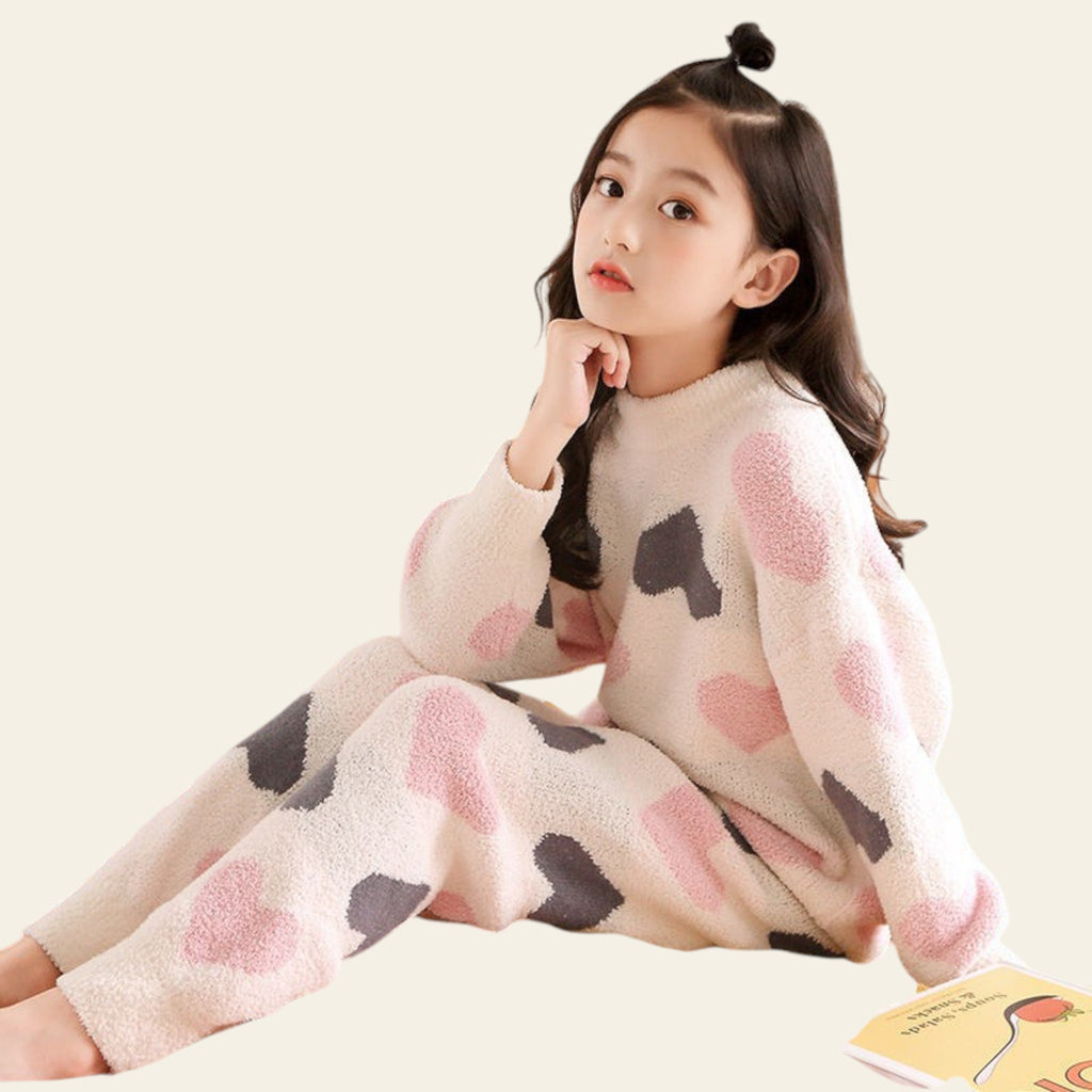 Young girl in a polka dot outfit sitting on a bed with a decorative headboard.