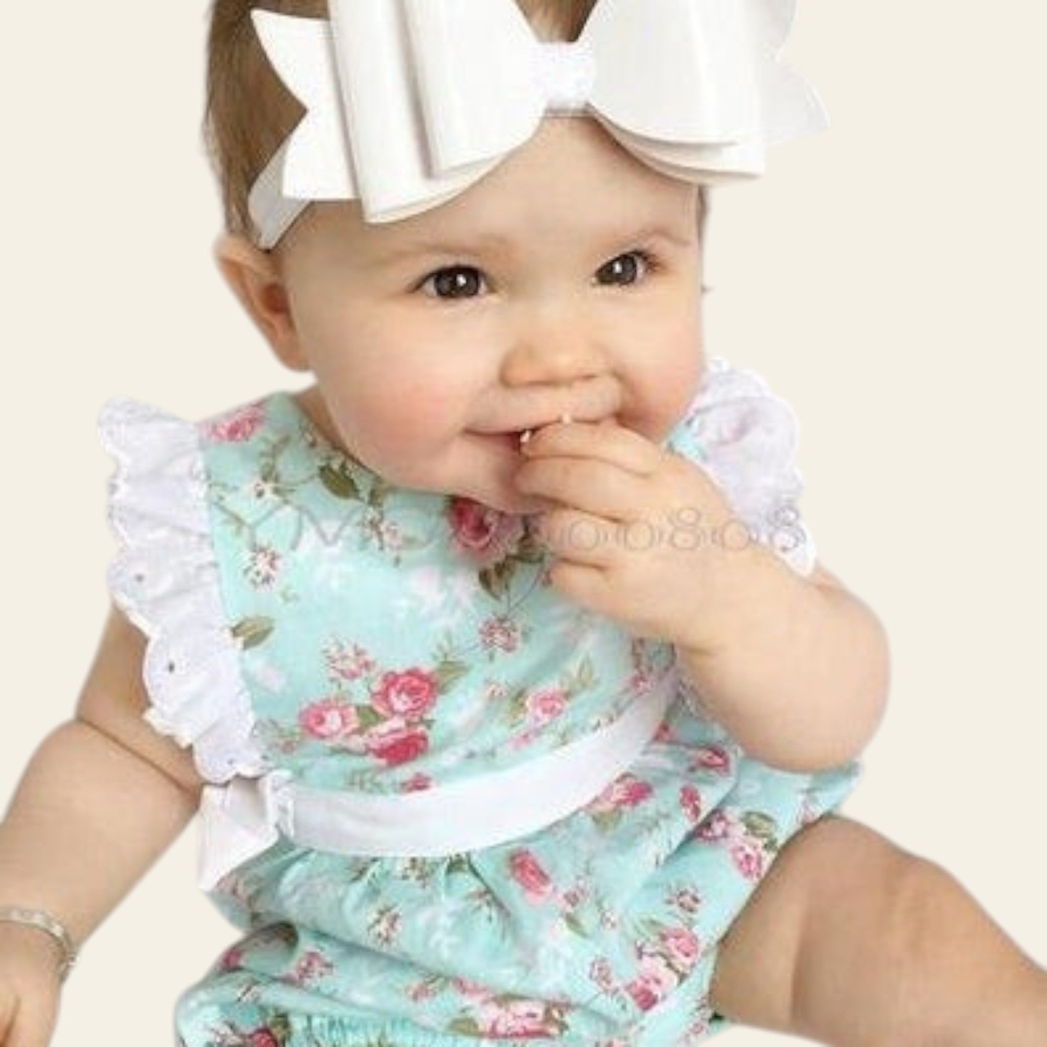 Baby wearing a floral romper with a large white bow on a plain background