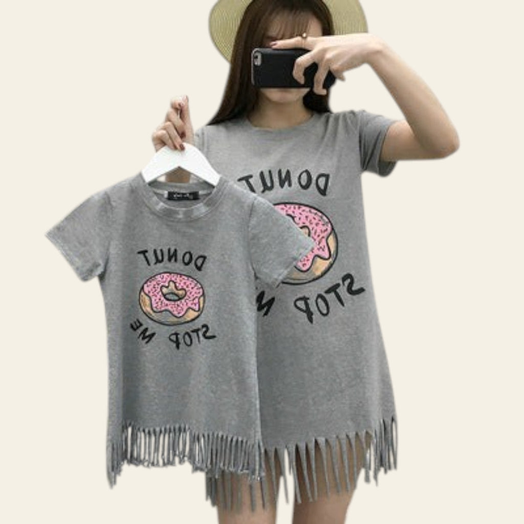 Person wearing a gray t-shirt with donut design and text, standing against a white brick wall.