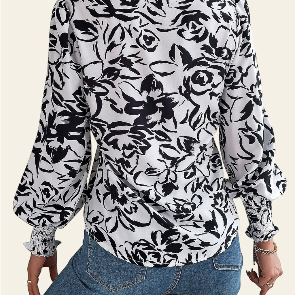 Person wearing a black and white floral blouse with blue jeans on a light background
