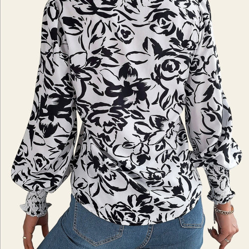Person wearing a black and white floral blouse with blue jeans on a light background