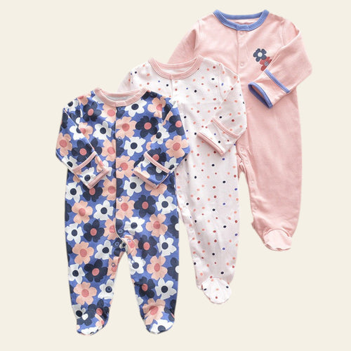Three baby onesies with floral, polka dot, and solid designs on a beige surface.