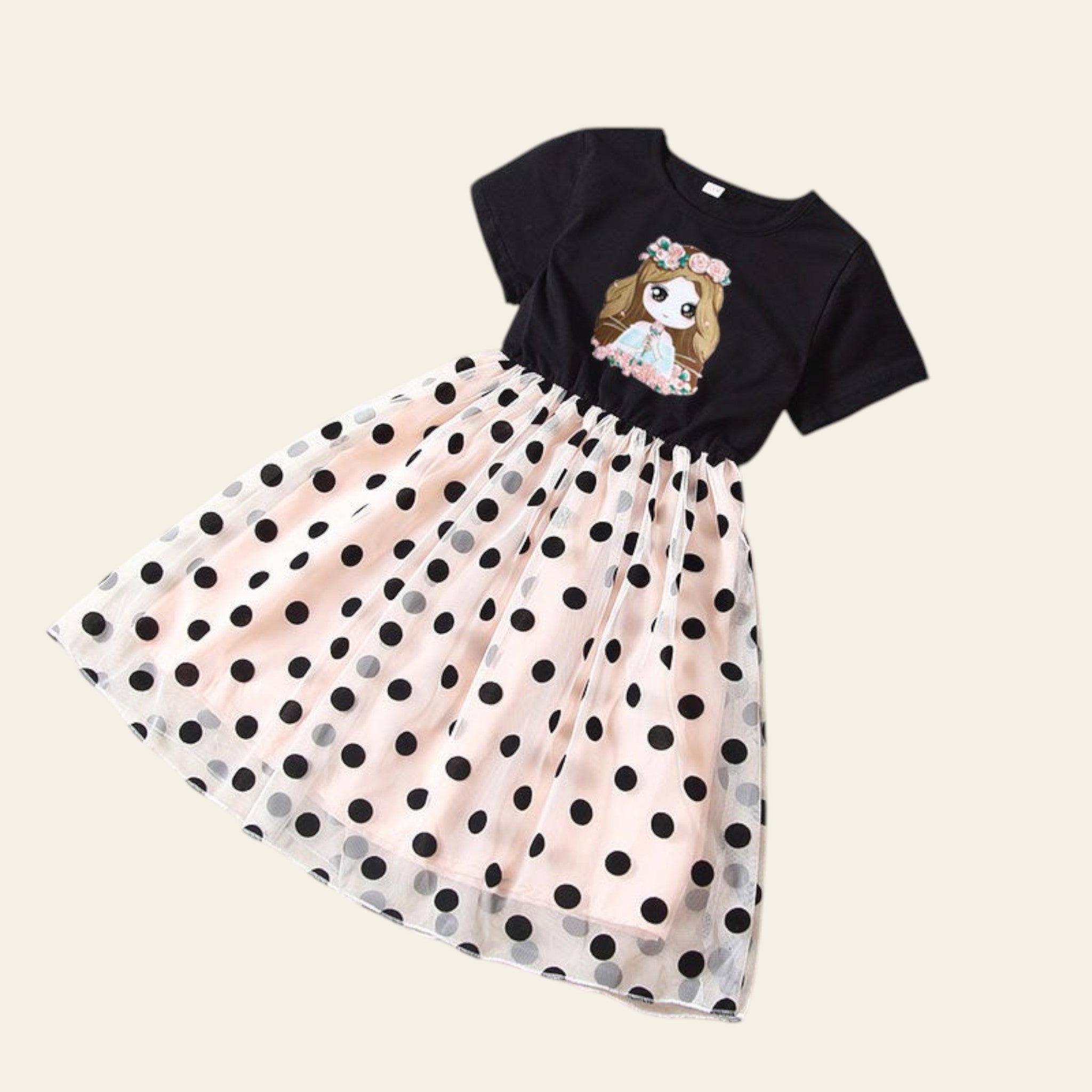Black top with a cartoon design and polka dot skirt on a beige surface.