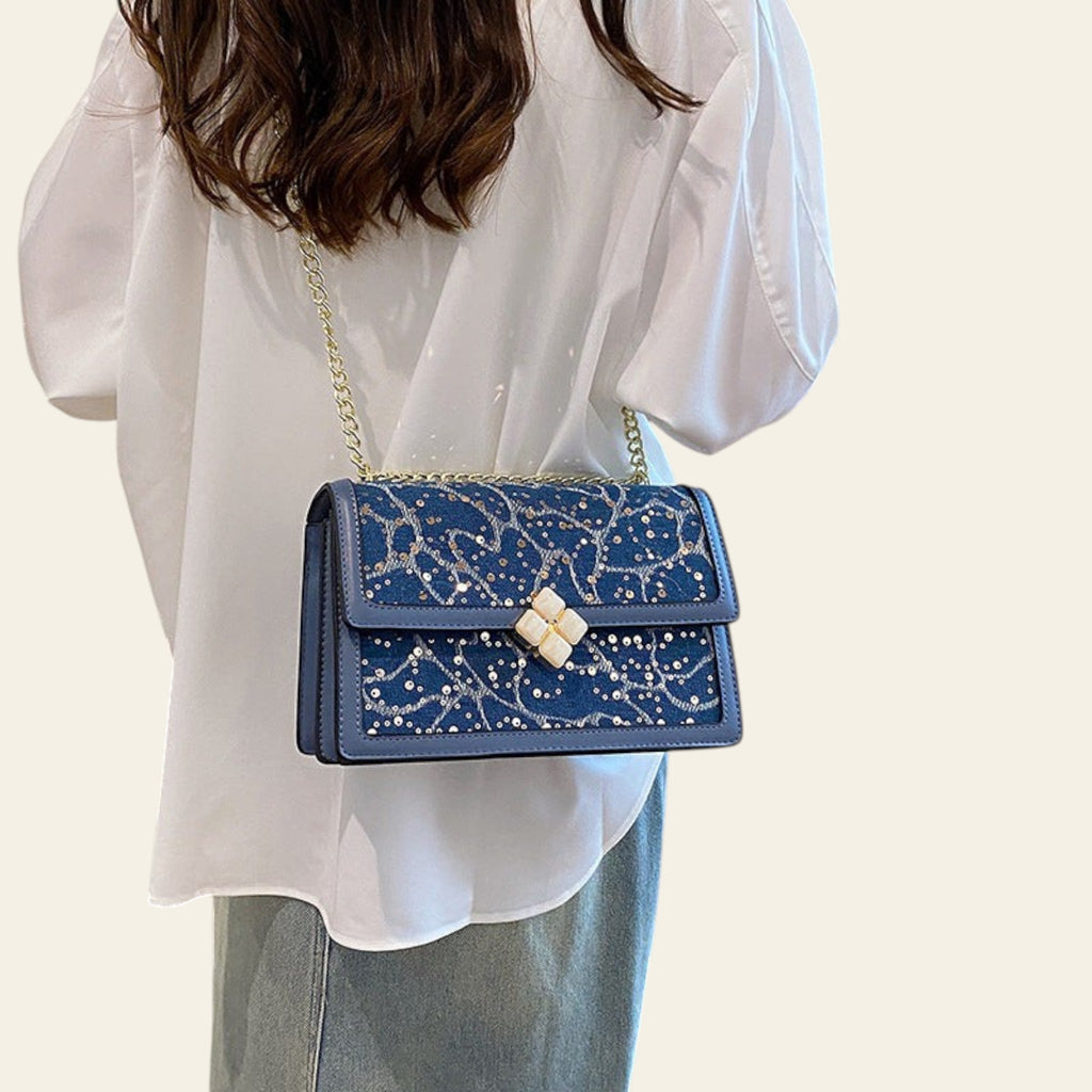 Person holding a blue handbag with floral patterns indoors.