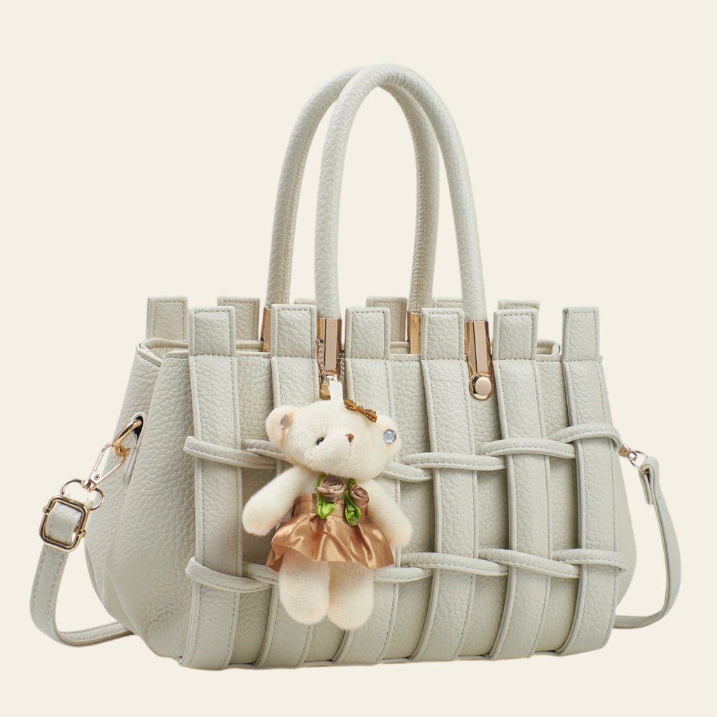 Light gray woven handbag with a teddy bear charm on a white background