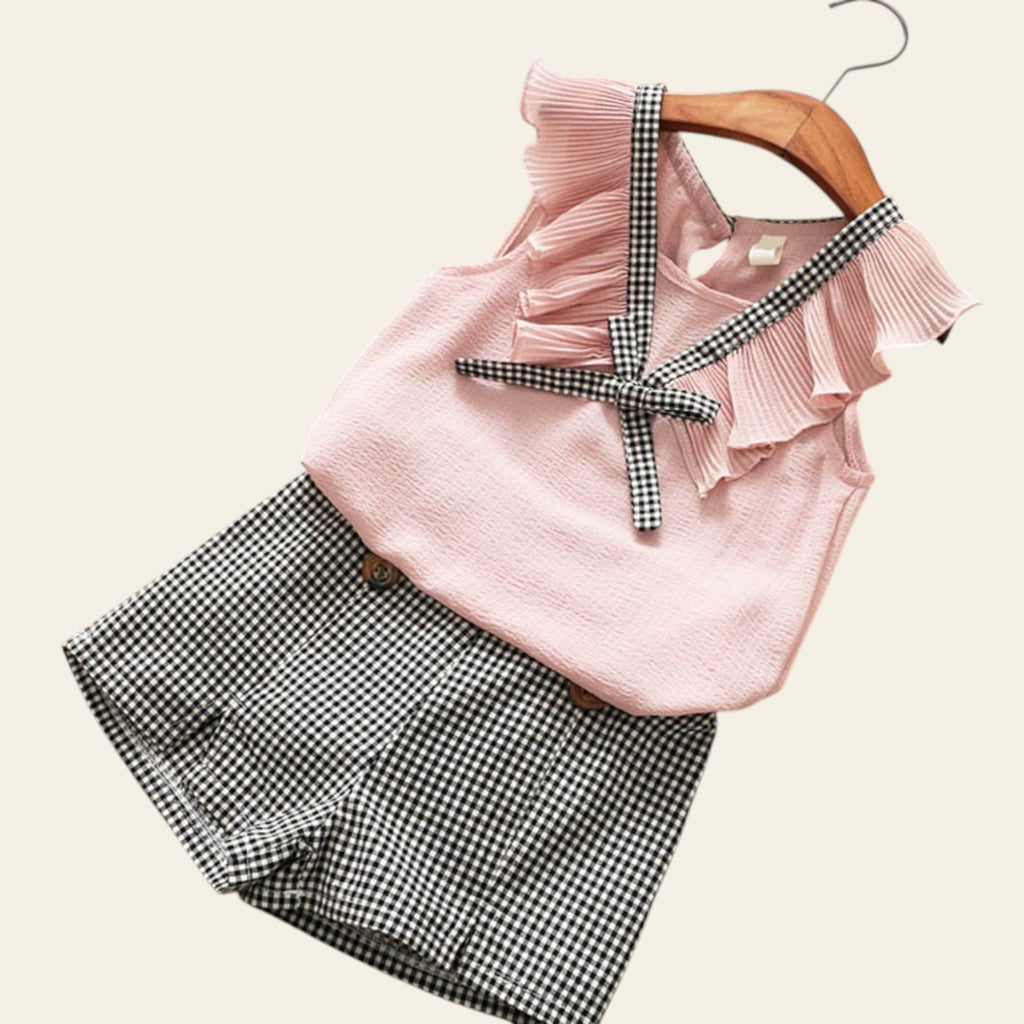 Pink ruffled top with plaid shorts on a wooden surface