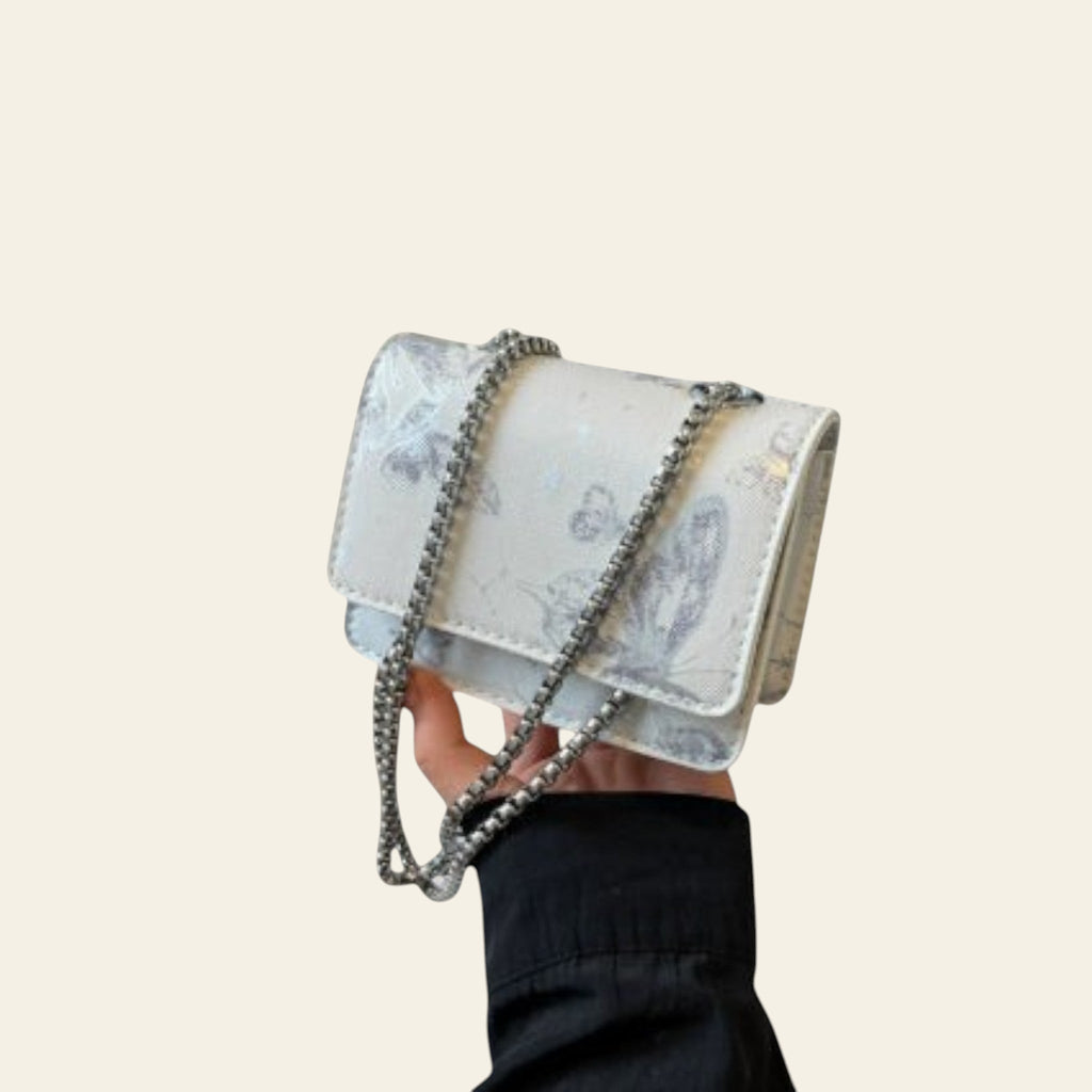 Hand holding a floral handbag with a chain detail, with a branded box in the background.