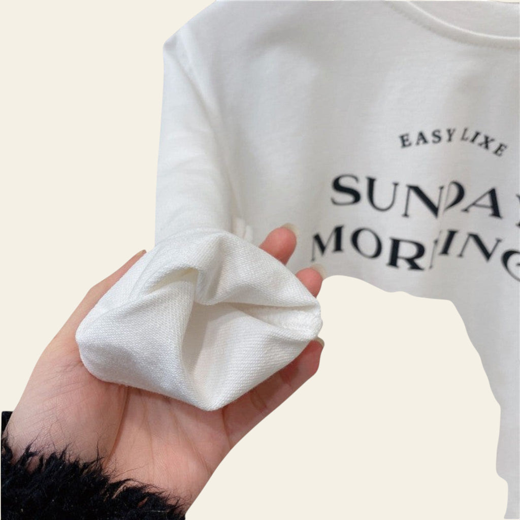 White sock held in a hand with a blurred background of a white shirt with text.