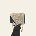 Hand holding a patterned handbag with a gold chain against a black background