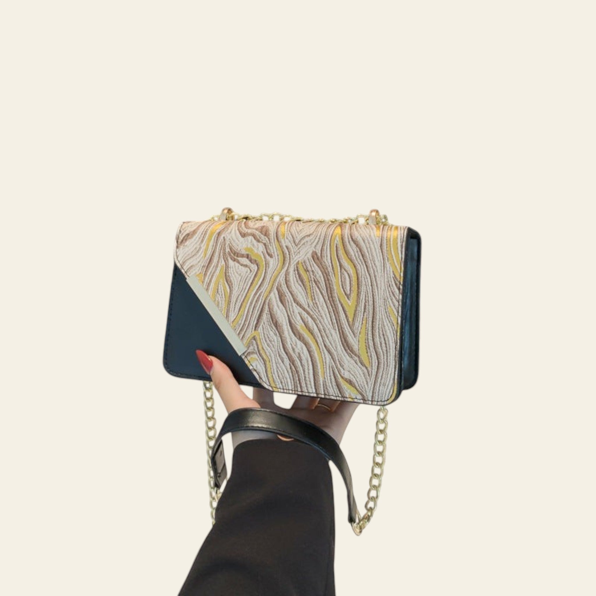 Hand holding a patterned handbag with a gold chain against a black background