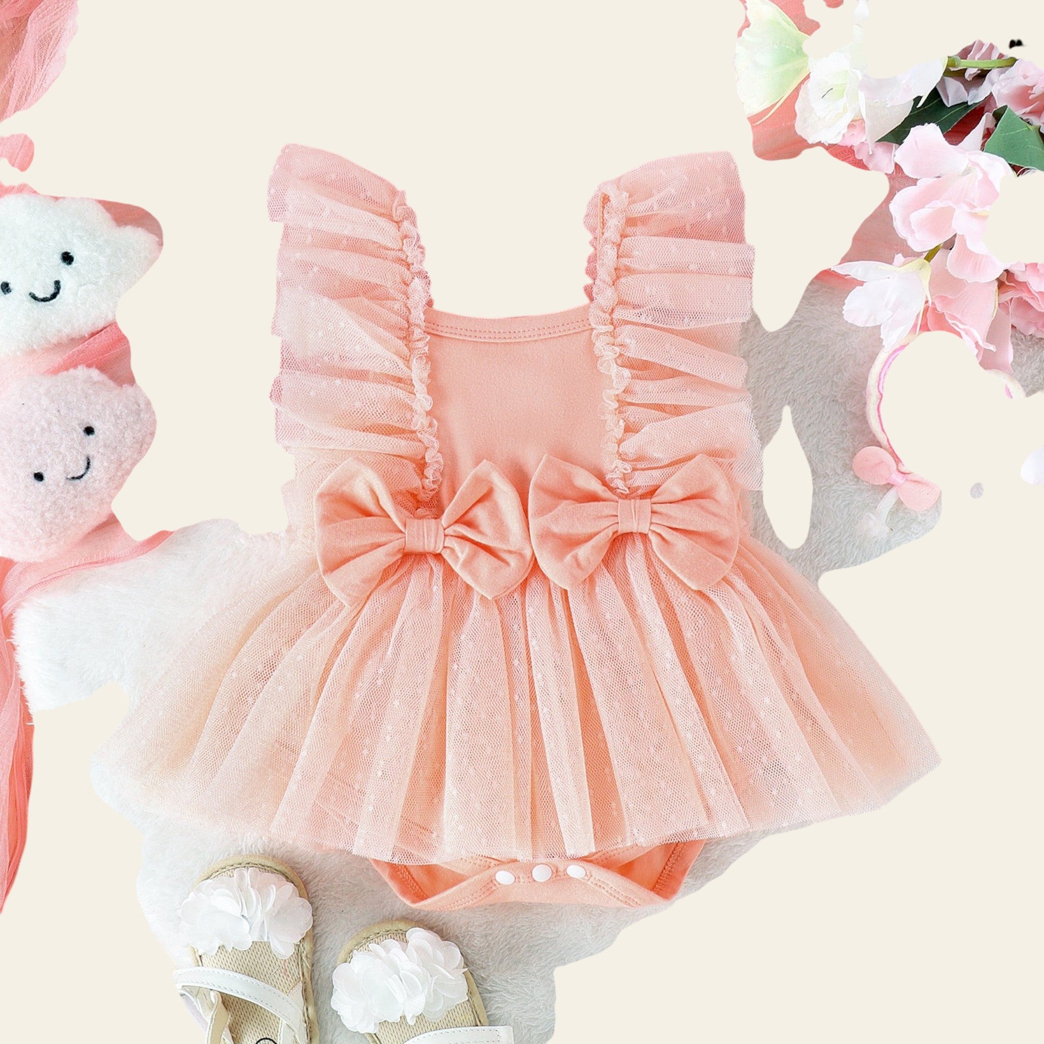Pink baby romper with ruffles and a bow, surrounded by flowers and toys on a light background