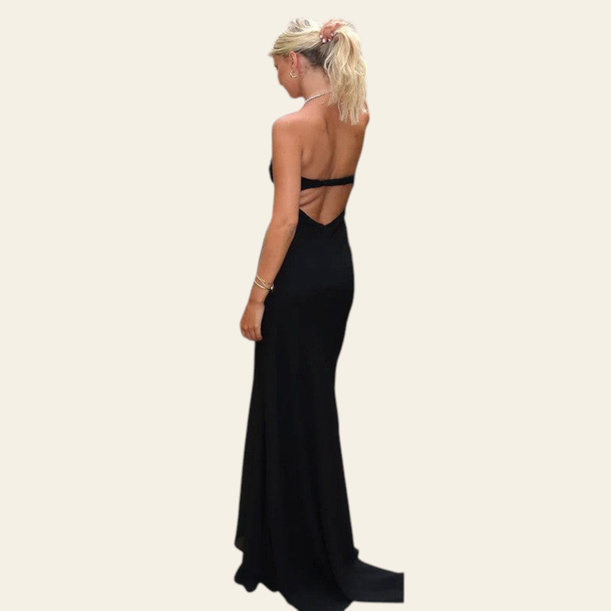 Woman in a black evening gown standing in an outdoor setting with greenery and a building.
