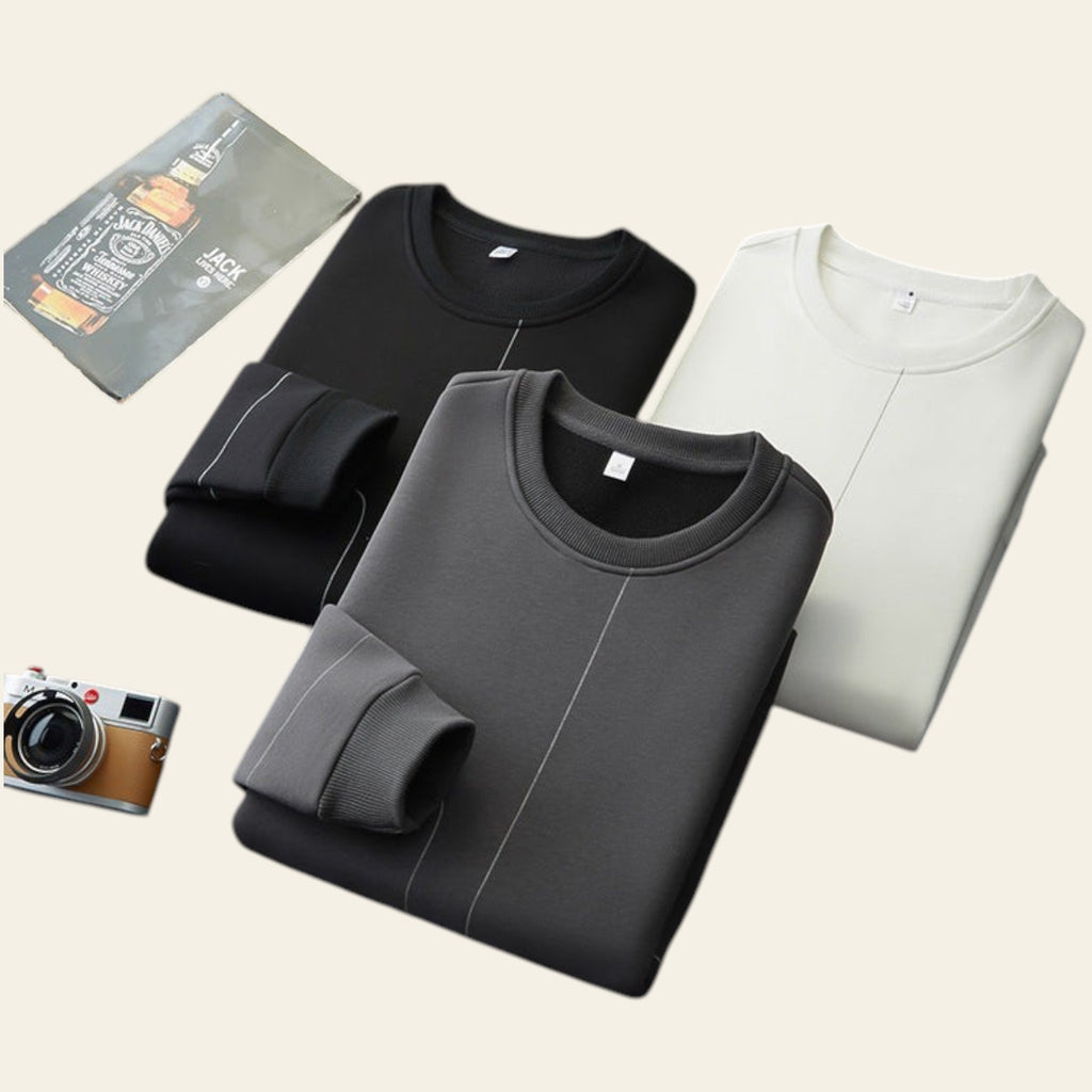 Folded crewneck sweatshirts in black, gray, and white on a gray surface