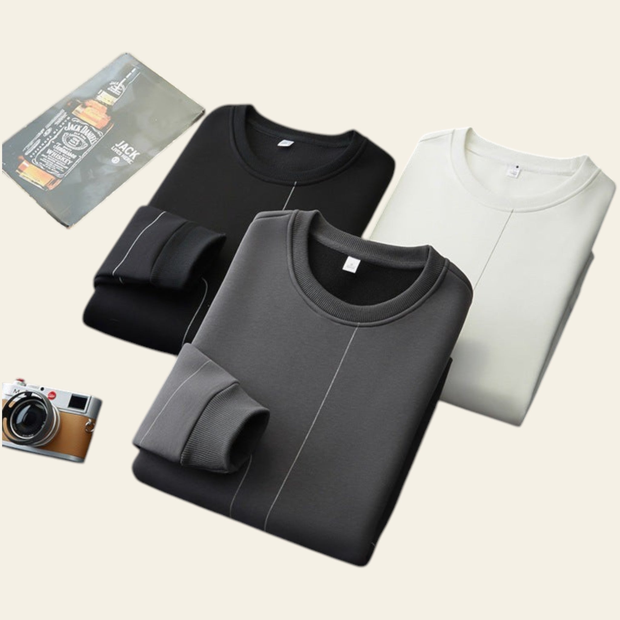 Folded crewneck sweatshirts in black, gray, and white on a gray surface