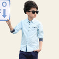 Young boy in a light blue shirt and dark pants holding a sign outdoors.
