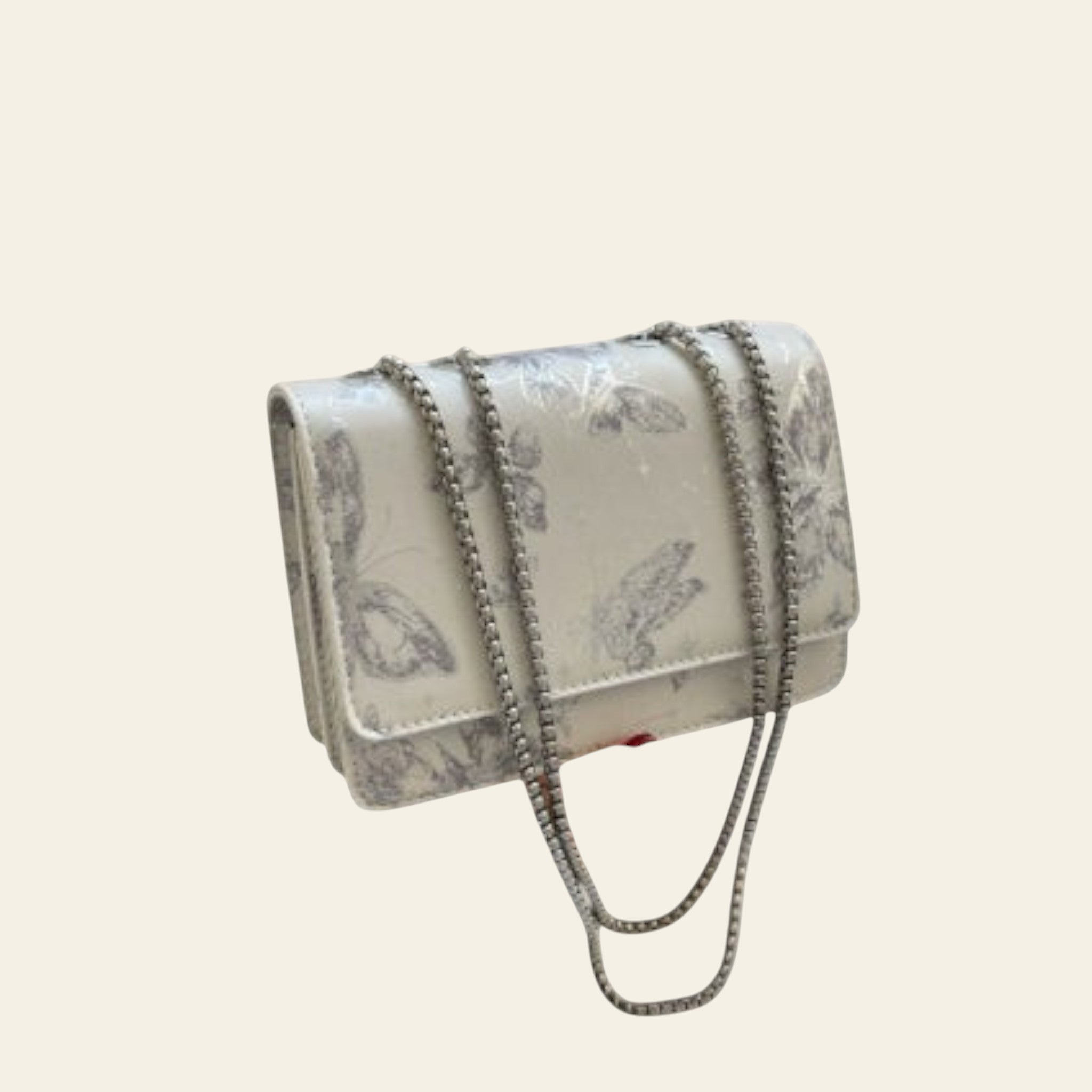 Silver floral handbag with chain detail held by a person, with a gray coat and glass of water in the background.