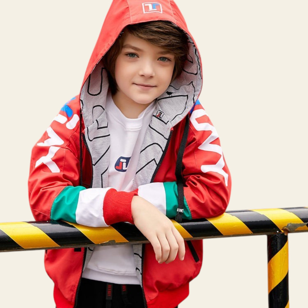 Child wearing a colorful jacket with a brand logo, standing behind a yellow and black striped barrier.