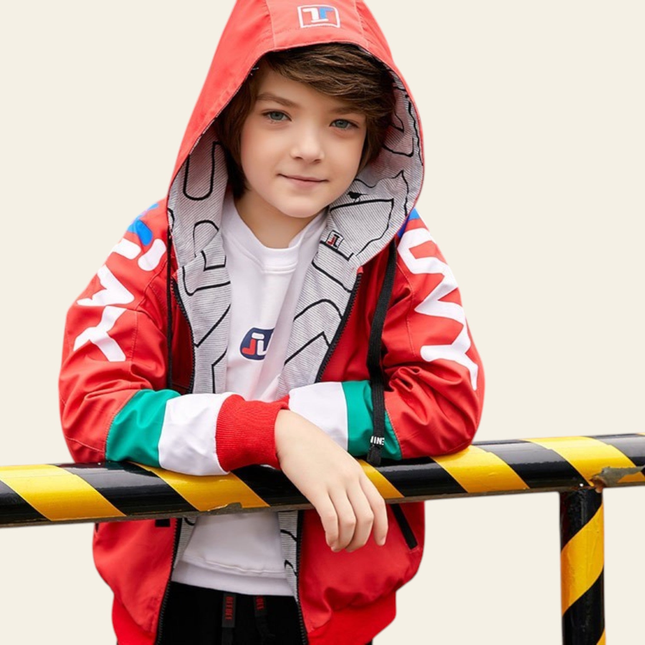 Child wearing a colorful jacket with a brand logo, standing behind a yellow and black striped barrier.