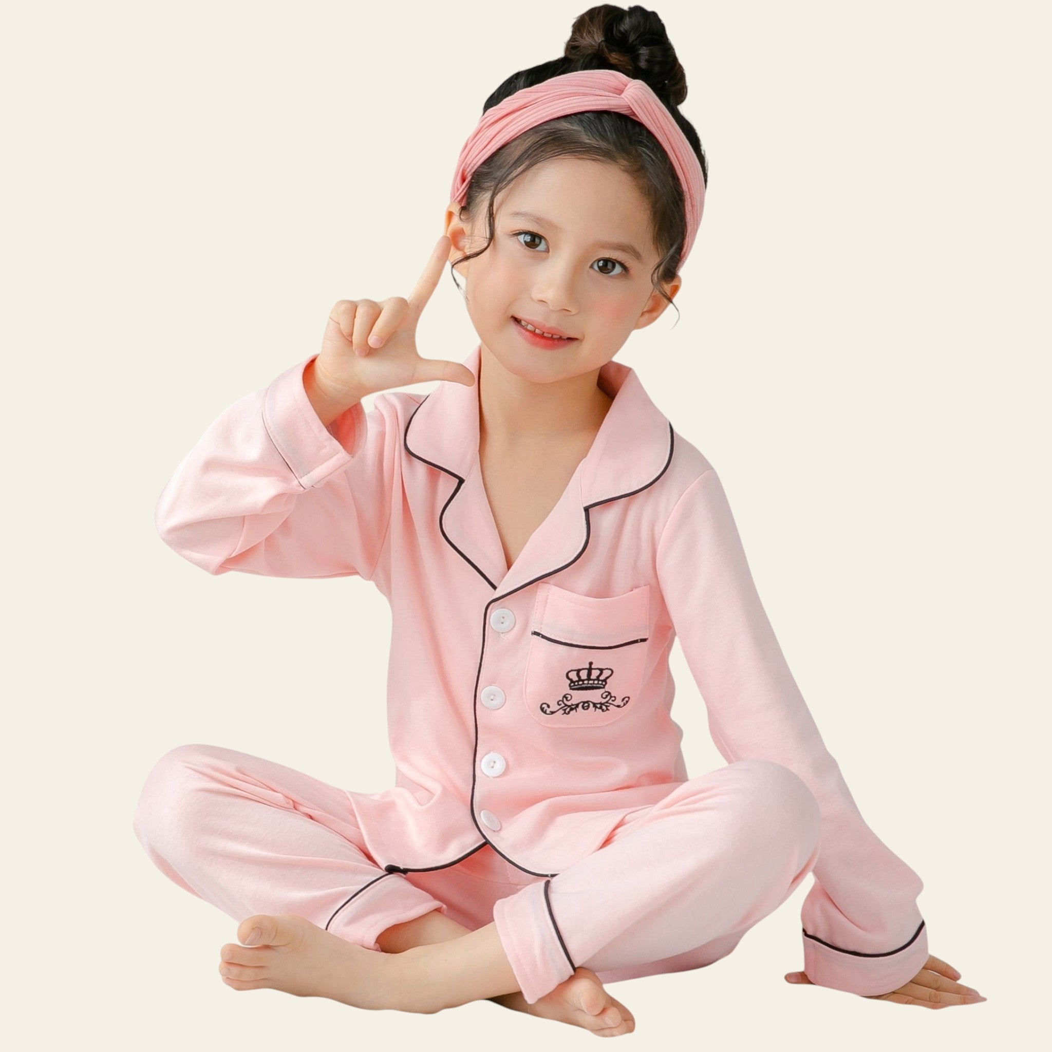 Child wearing pink pajama set with a headband, sitting on a bed.