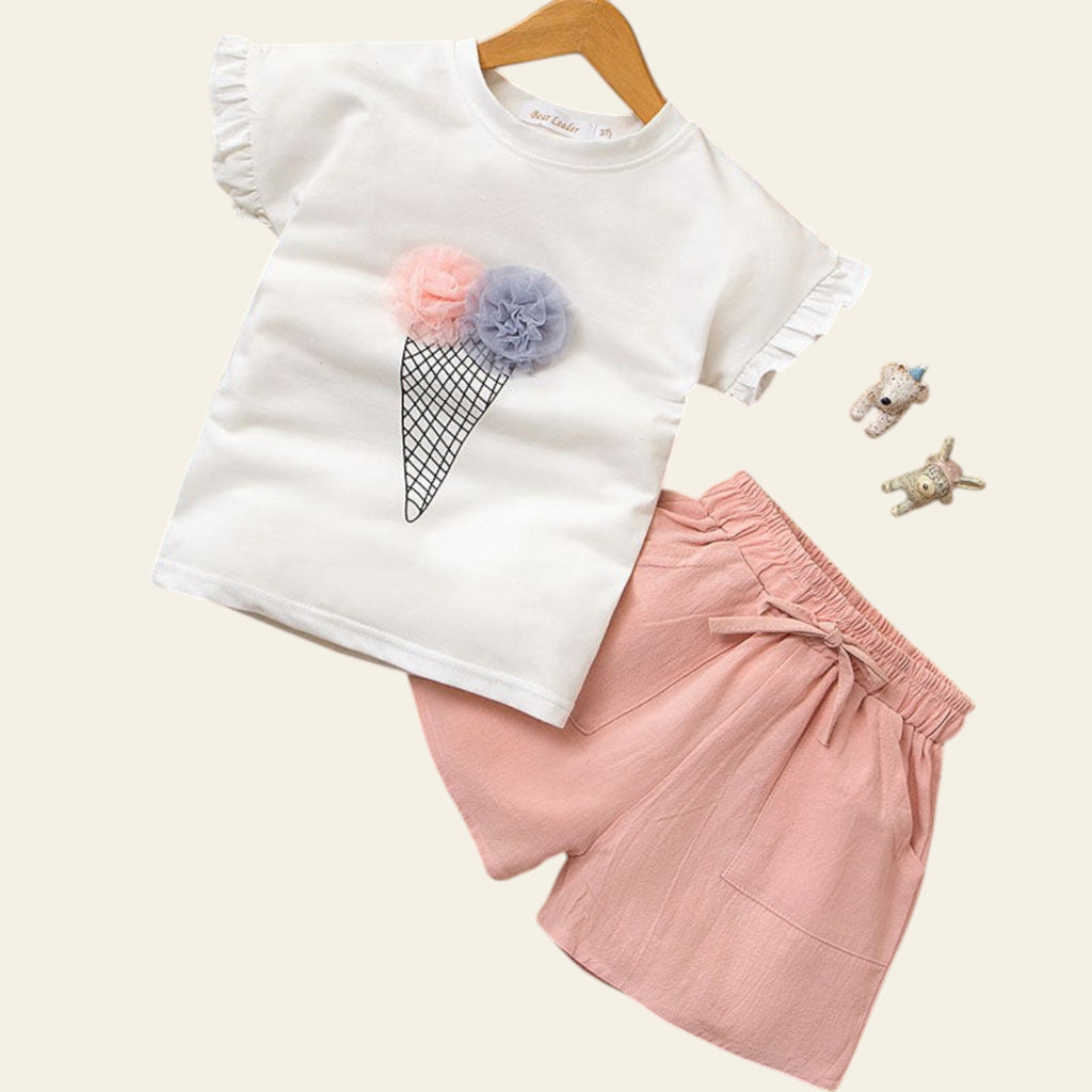 White t-shirt with ice cream cone design and pink shorts on a wooden surface.