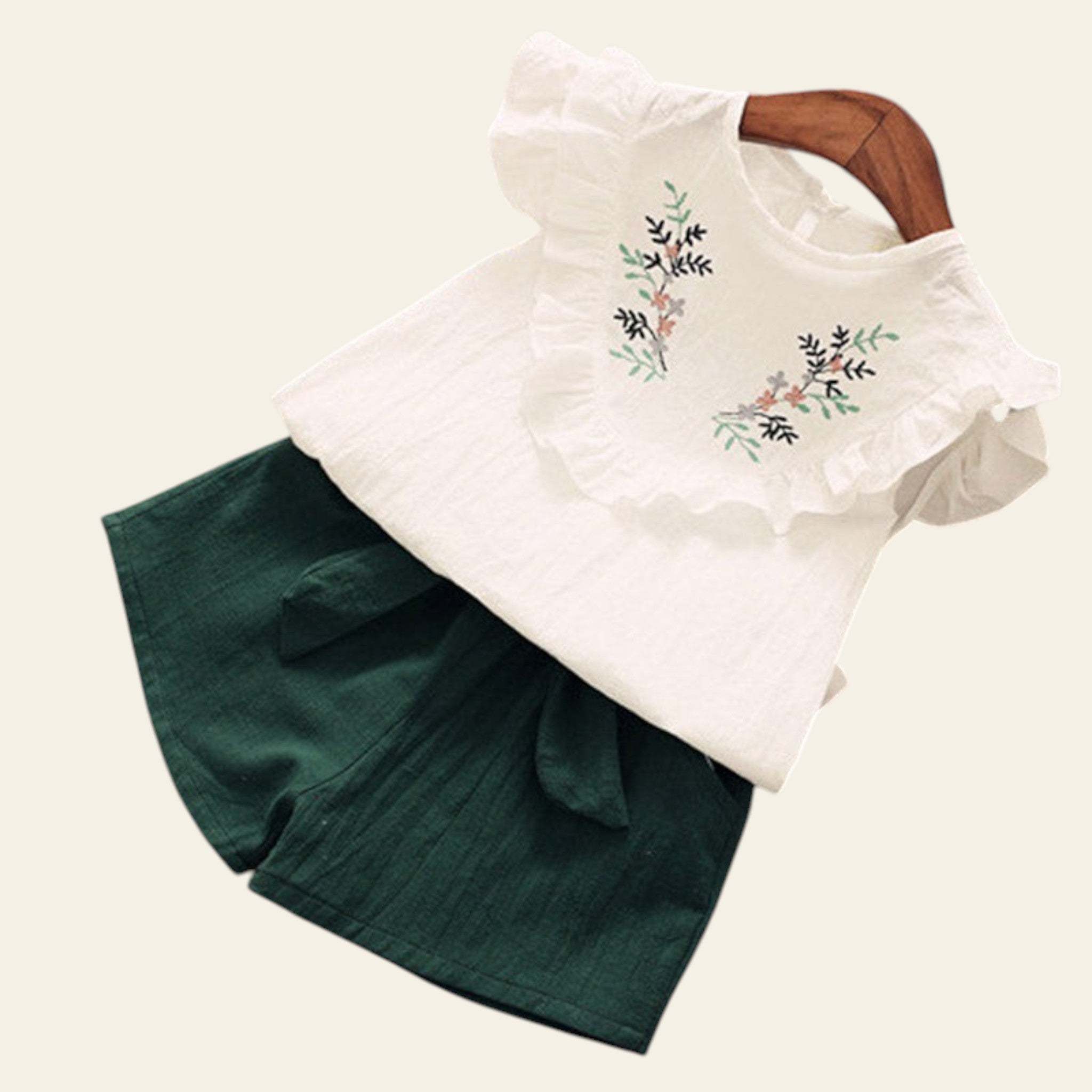 White blouse with floral embroidery and green shorts on a wooden surface