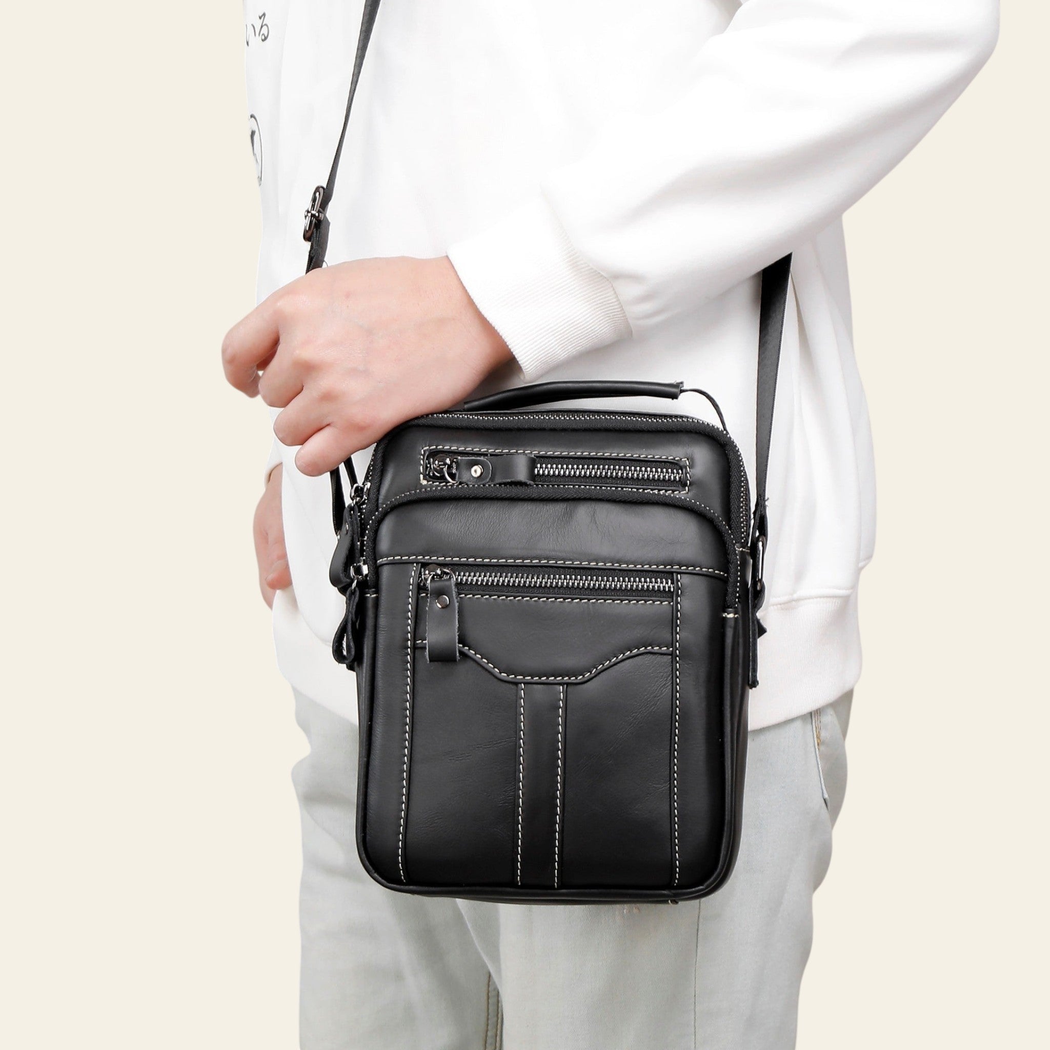 Person holding a black leather crossbody bag against a neutral background