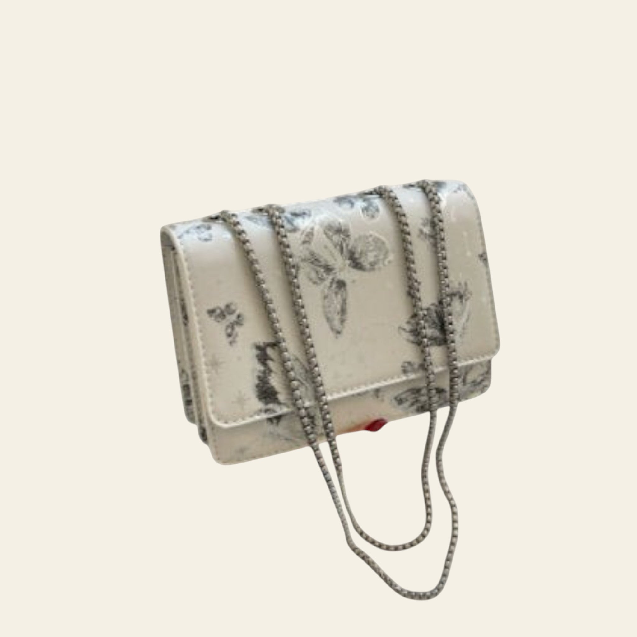 Handbag with floral pattern held by a person, with a book and glass in the background.