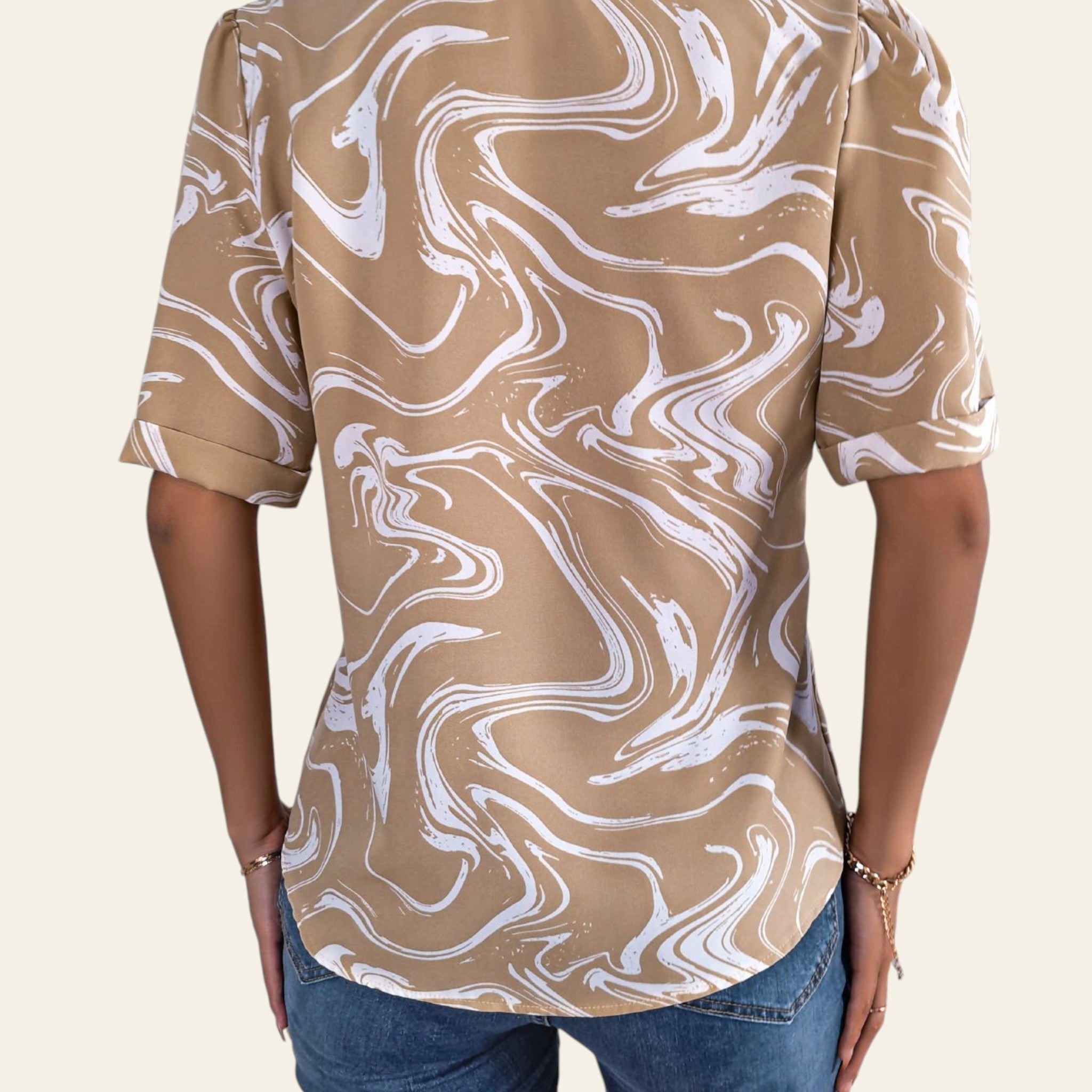 Person wearing a beige and white marbled pattern shirt with blue jeans indoors.