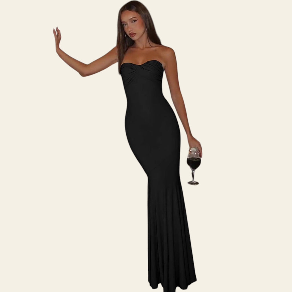 Woman in a black strapless gown holding a glass of wine in a bathroom setting.